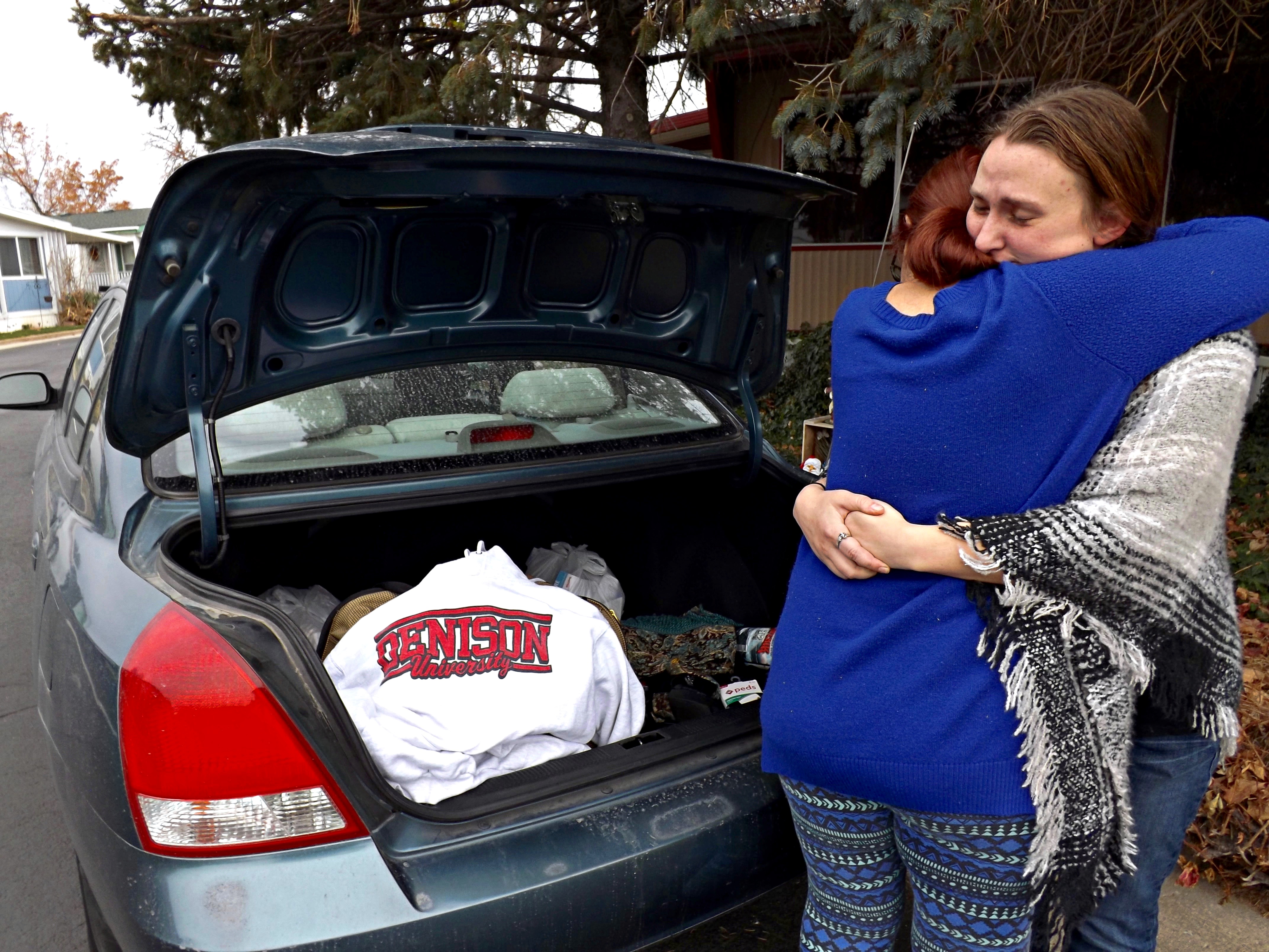 A student is hugging a parent in front of an open car trunk showing a university sweater and moving boxes.