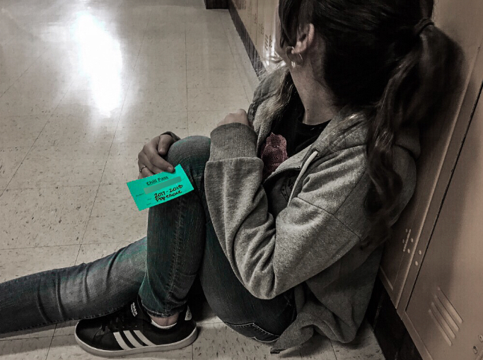 A student sits in an empty hallway, showing a bright blue chill pass.